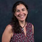light-skinned appearing woman with long brown hair in front of a grey background