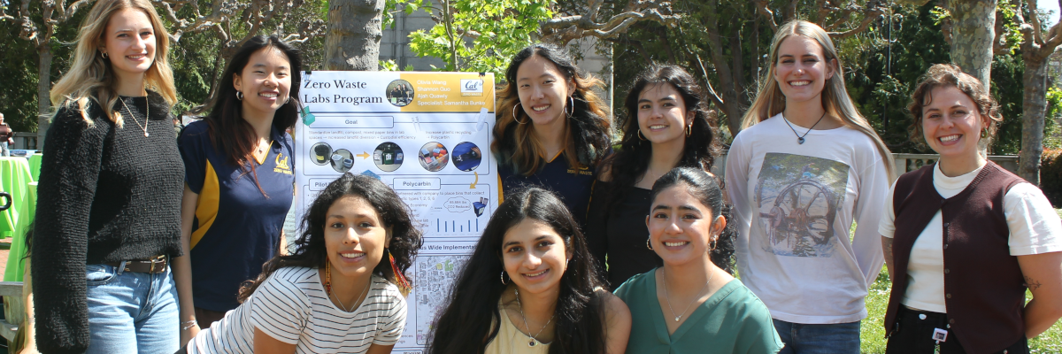 Nine people huddled around a board that says "Zero Waste Labs Program".